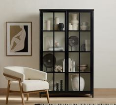 a white chair sitting in front of a black book shelf filled with books and vases