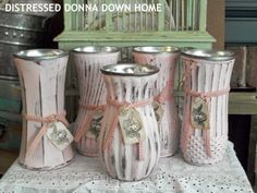 four pink vases sitting on top of a white doily covered table with ribbon tied around them