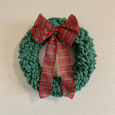 a green wreath with red and white plaid bow hanging on the wall in front of a white wall