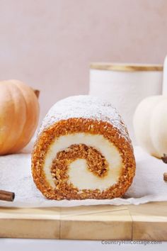 a cinnamon roll is cut in half and sitting on a cutting board next to some pumpkins