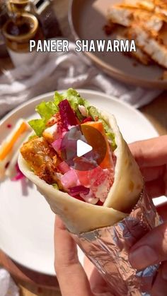 a person holding a wrap filled with meat and veggies on top of a white plate