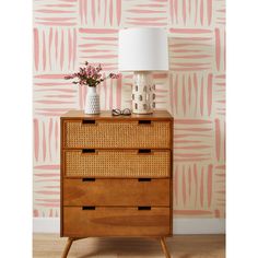 a wooden dresser sitting next to a lamp on top of a hard wood floor covered in pink and white wallpaper