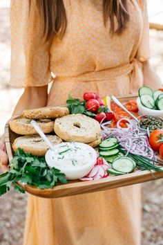 a woman in a yellow dress holding a tray full of vegetables and pretzels