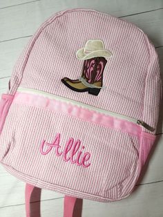 a pink and white backpack with a cowboy boot embroidered on the front, sitting on a wooden floor