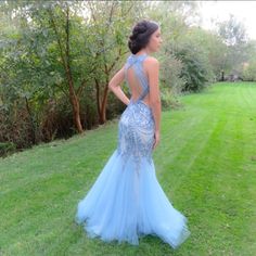 a woman is standing in the grass wearing a blue dress with an open back and beading on it