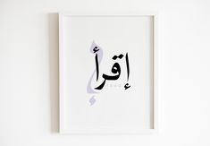 an arabic calligraphy is displayed in a white frame on the wall next to a plant