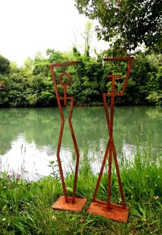 two metal sculptures in the grass near water