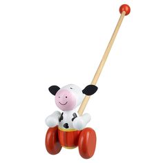 a toy cow sitting on top of a red drum with a wooden stick in its mouth