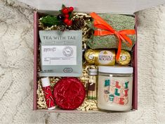 an open box with tea, cookies and other items in it on a white blanket