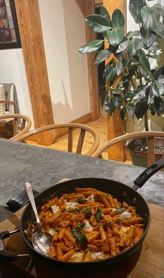 a skillet filled with pasta sitting on top of a table next to a potted plant