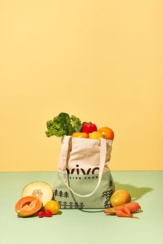 a bag full of fruits and vegetables sitting on top of a blue table next to a yellow wall