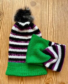 two knitted hats sitting on top of a wooden floor next to each other, one with a pom - pom