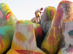 a man painting rocks with multicolored paint on the ground and sky in the background