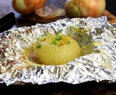 an onion on tin foil with other food items in the backgroung behind it