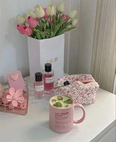 a white table topped with pink and white flowers next to a vase filled with tulips