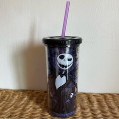 a cup with a purple straw in it sitting on a wicker table next to a wall