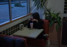 a woman sitting at a table with a drink in her hand and looking out the window