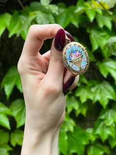 A charming and enduring trend from the Victorian Era was the custom of the Language of Flowers, wherein every blossom and leaf imaginable held secret meaning. It was so commonly practiced that floral messages were incorporated into jewelry, with our locket serving as such an example. Crafted in 14 karat yellow gold, a colorful bouquet in a jardiniere rests atop a bright turquoise background. The featured flowers include pink roses, meaning 'bashful love' as well as purple, blue and red cosmos me Oval Enamel Jewelry For Wedding, Oval Enamel Wedding Jewelry, Vintage Yellow Gold Jewelry With Birth Flower, Vintage Enamel Keepsake Jewelry, Antique Hand Painted Jewelry Gift, Antique Hand Painted Jewelry For Gifts, Antique Hand Painted Jewelry For Gift, Cosmos Meaning, Roses Meaning