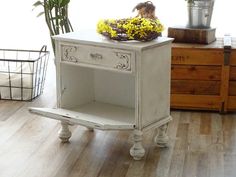 a small white table with flowers on top and a potted plant next to it