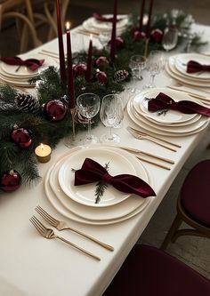 the table is set with white plates and red napkins, silverware, pine cones, evergreen branches, candles, and christmas decorations