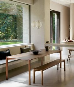 a table and bench in a room with large windows