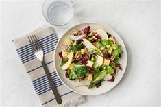 a white plate topped with an apple salad next to a fork and glass of water