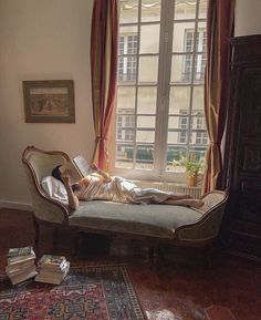 a person laying on top of a couch in front of a window next to a book shelf