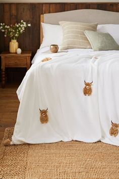 a bed with white sheets and two brown cows on it's head embroidered onto the covers