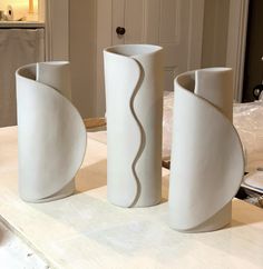 three white vases sitting on top of a table next to each other in a room