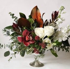 a vase filled with flowers and greenery on top of a white tablecloth covered floor