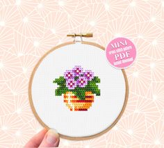 a cross stitch flower pot with purple flowers in it