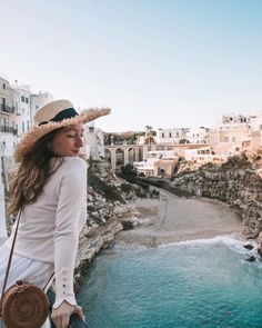 a woman standing on top of a cliff next to the ocean wearing a straw hat