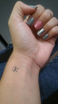 a woman's wrist with a smiley face tattoo on the left side of her arm