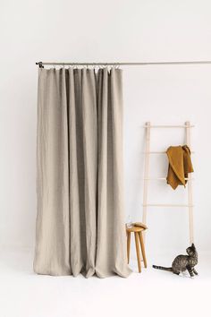 a cat sitting in front of a curtain next to a ladder and chair with a towel on it