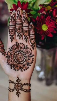 a woman's hand with henna tattoos on it and flowers in the background