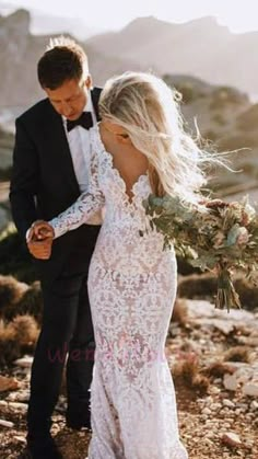 a bride and groom standing in the desert holding each other's hands while looking at their phone