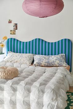 a bed with blue and white striped headboard next to a pink light fixture above it