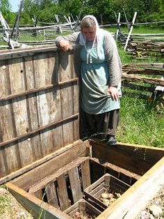 an old woman standing next to a wooden box in the grass and looking into it