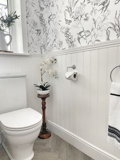 a white toilet sitting in a bathroom next to a wall with flowers and towels on it