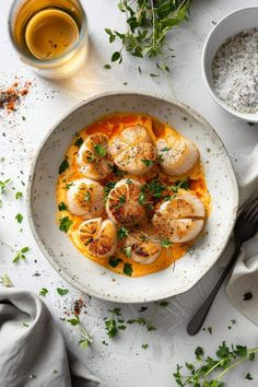 a white bowl filled with cooked scallops on top of a table next to silverware