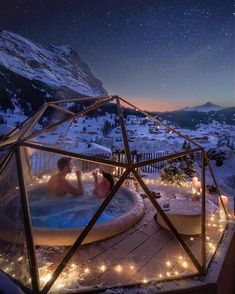 a hot tub in the middle of a snowy mountain with people sitting inside it at night