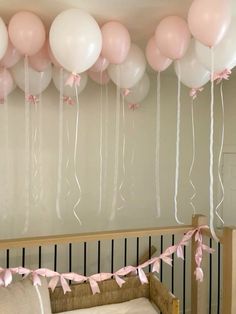 pink and white balloons hanging from the ceiling above a crib