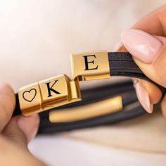 a person holding a black and gold bracelet with letters on it