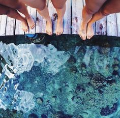 two people standing on a dock with their feet in the water and one person's reflection