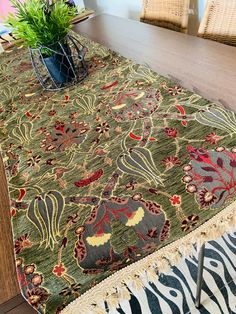 a table with a rug on top of it and a plant in a vase next to it