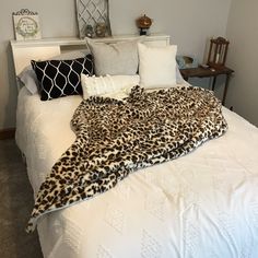 a leopard print blanket is on top of a white bed with pillows and throw blankets