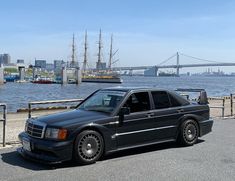 a black car parked in front of a large body of water with a bridge in the background