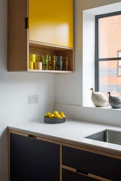 two birds sitting on the window sill next to some lemons and cups in a bowl