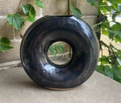 a black vase sitting on top of a table next to a brick wall and green plants