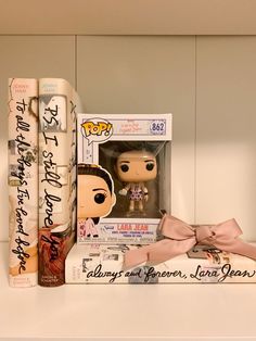 two pop vinyls are sitting on top of some books, one is pink and the other is white